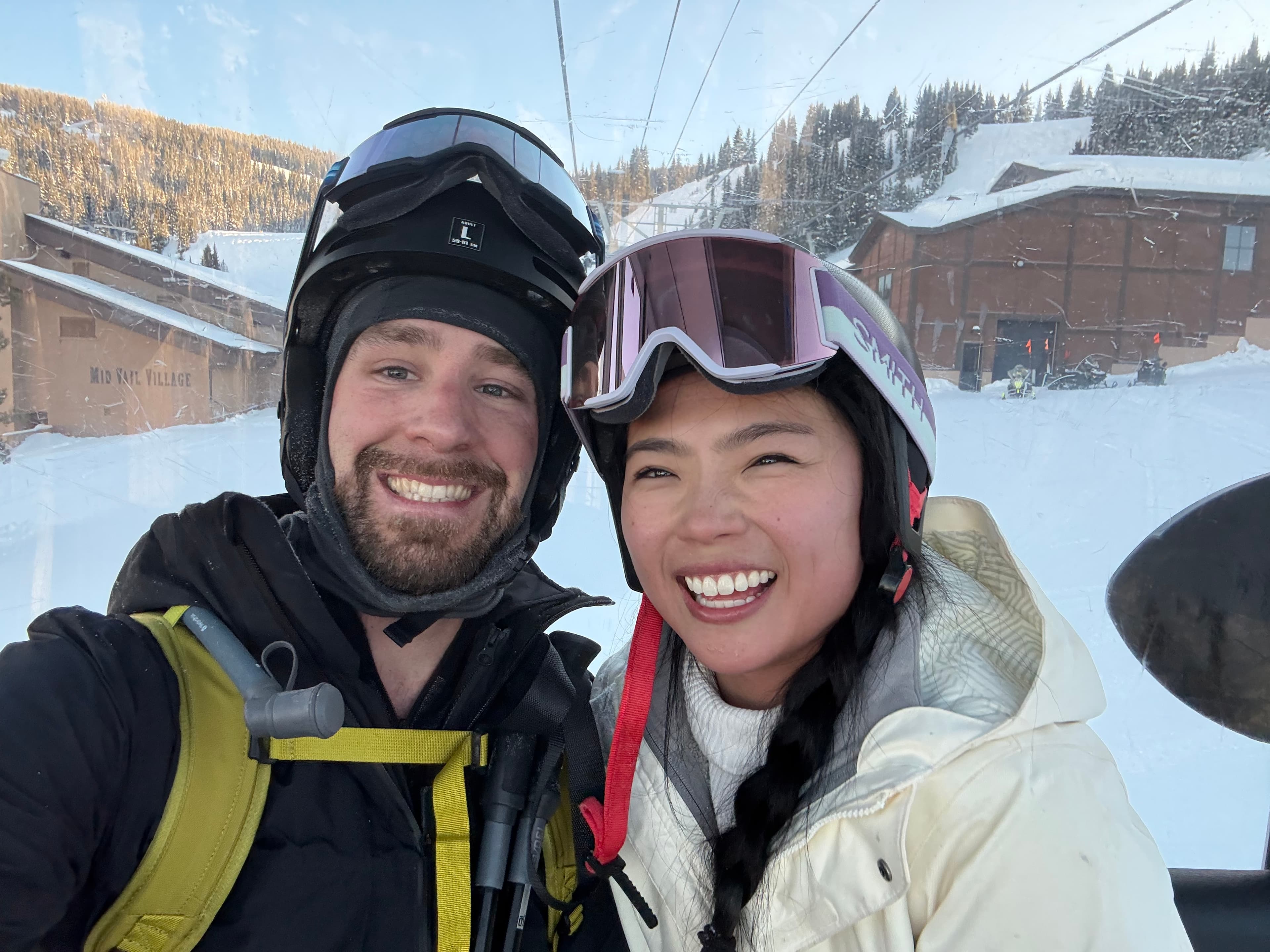 A photo of me and my wife on a ski lift in snow clothes, helmets, and ski goggles