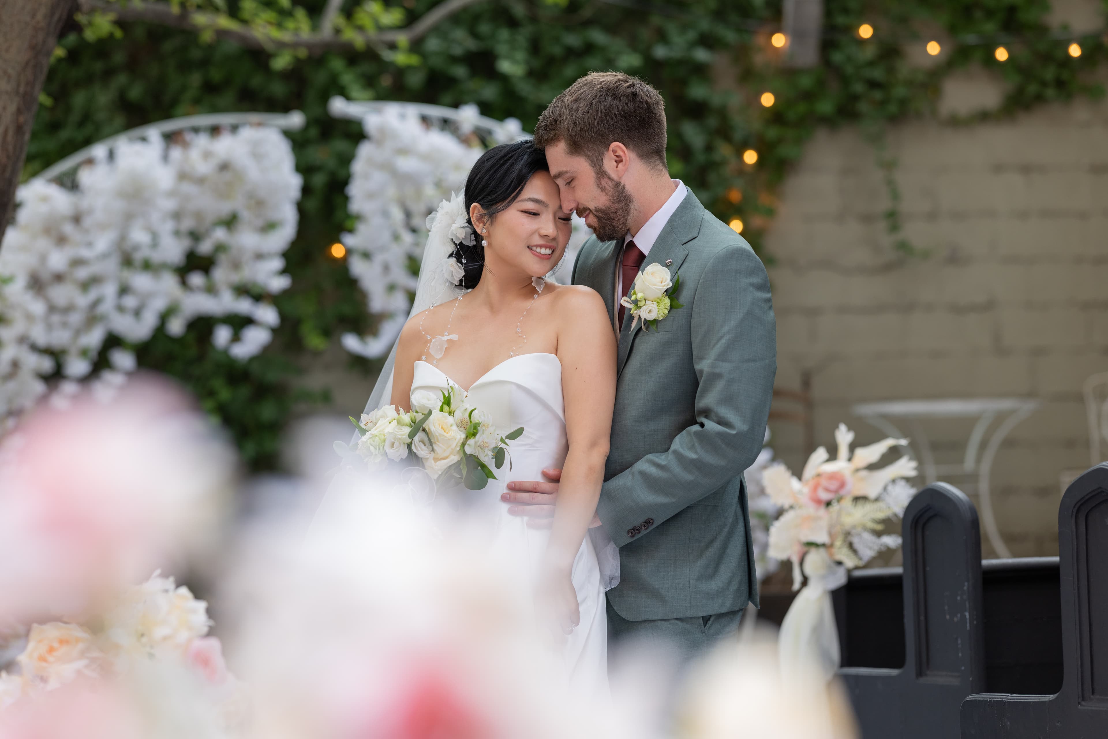A photo of me and my wife in a suit and wedding dress at our wedding ceremony with green ivy in the background